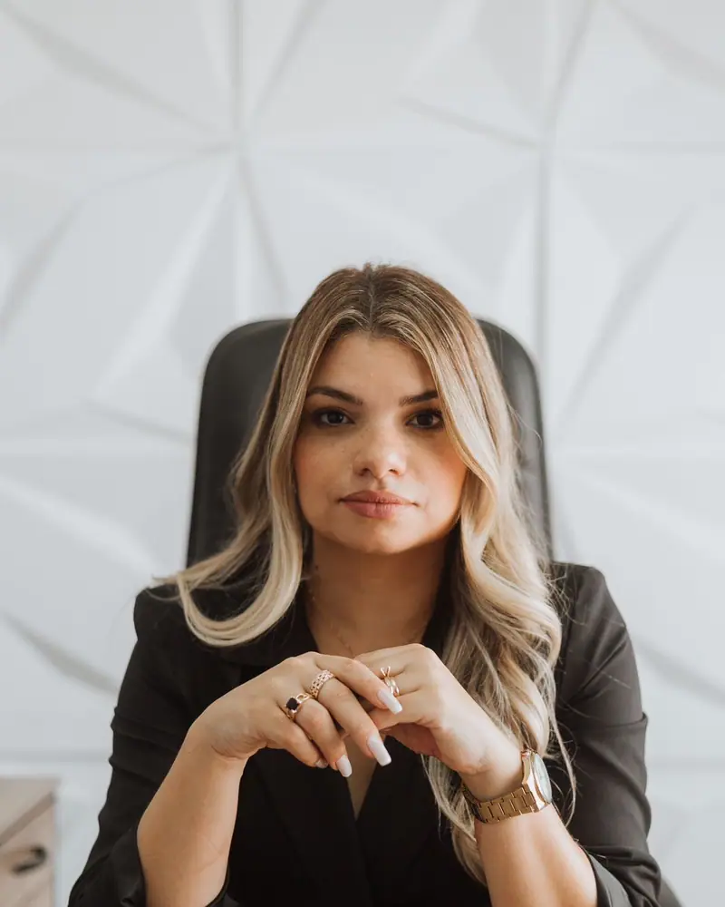 Dra. Camila Chagas à mesa do escritório, de blazer preto