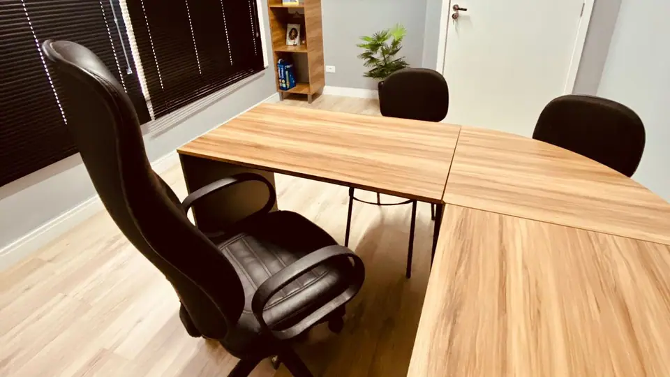 Sala de atendimento do escritório, com mesa em L, cadeira e estante